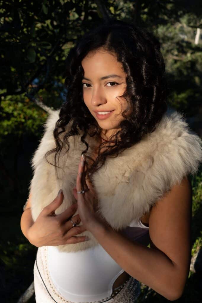 Tantra Massage Los Angeles - Temple of Bliss Pregnant woman with curly hair wearing a fluffy fur stole outdoors, hands resting on her belly and smiling.